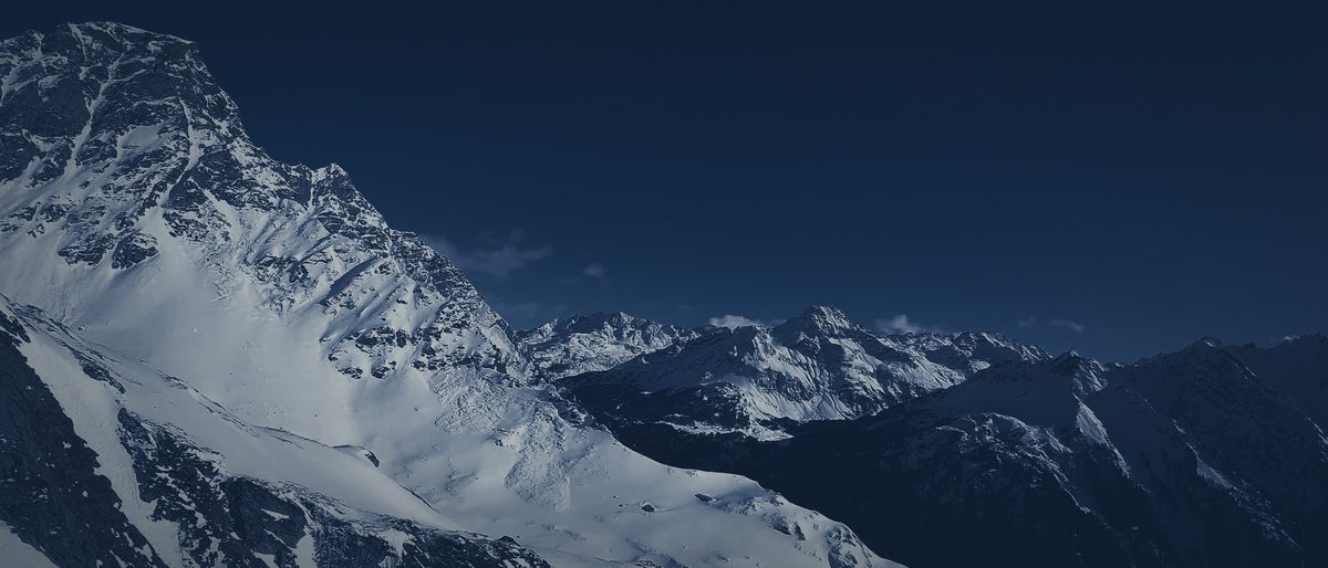Snow-covered mountain peaks at night, a long ridge under a dark sky.