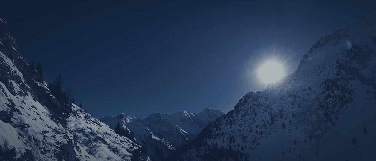 A mountain valley at night between snowy slopes, a low light over the far ridge.